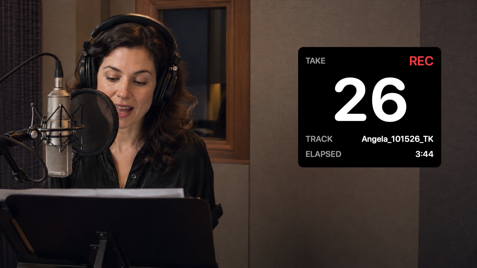 A voice actor at the microphone in a recording booth, with SessionHUD's panel beside her showing take 26, recording, track Angela_101526_TK, elapsed 3:44.